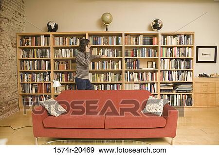 Stock Photo - Side profile of a young man leaning against a bookshelf and talking on a mobile phone. Fotosearch