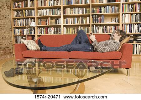 Side profile of a young man lying on a couch and reading a book View Large Photo Image Stock Image - Side profile of a young man lying on a couch and reading a book. Fotosearch