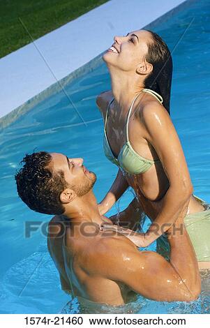 Stock Image - Side profile of a young man picking up a young woman in a swimming pool. Fotosearch