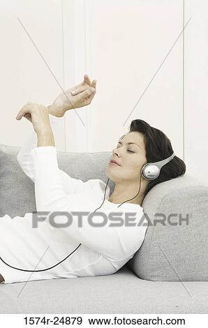 Side profile of a young woman wearing headphones listening to music on a couch View Large Photo Image Stock Photo - Side profile of a young woman wearing headphones listening to music on a couch. Fotosearch