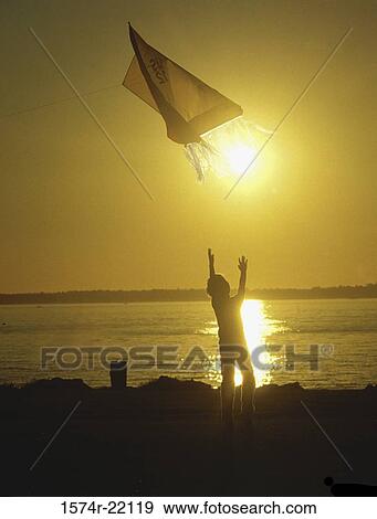 Stock Photo - Silhouette of a boy flying a kite at the beach. Fotosearch
