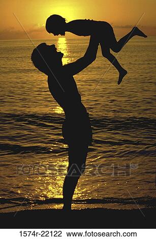 Stock Image - Silhouette of a father lifting his son at the beach. Fotosearch