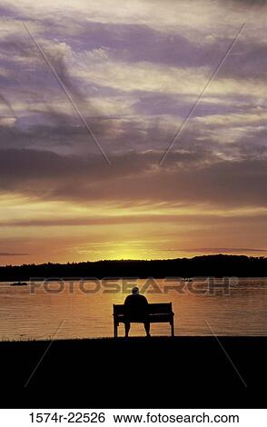 Silhouette of a person sitting on a bench during sunset View Large Photo Image Stock Photograph - Silhouette of a person sitting on a bench during sunset. Fotosearch