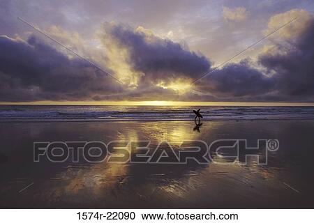 Silhouette of a person walking on the beach holding a surfboard View Large Photo Image Stock Image - Silhouette of a person walking on the beach holding a surfboard. Fotosearch