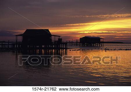 Stock Image - Silhouette of houses on the ocean at sunset. Fotosearch