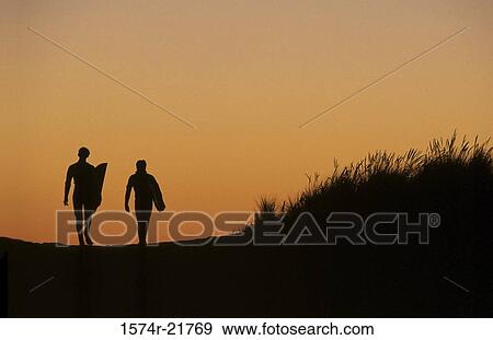 Silhouette of two people walking holding surfboards View Large Photo Image Stock Photo - Silhouette of two people walking holding surfboards. Fotosearch