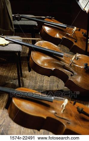 Stock Image - Three violins resting against chairs. Fotosearch