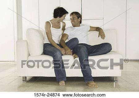 Picture - Young couple sitting on a couch and looking at each other. Fotosearch