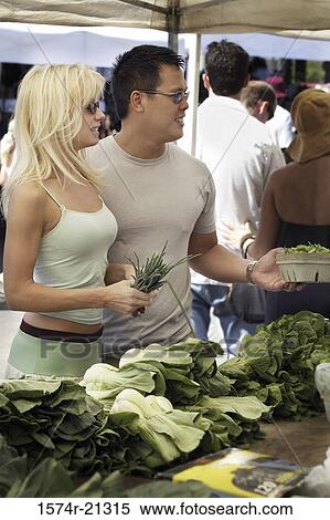 Stock Photography - Young couple standing at a market stall in a vegetable market. Fotosearch