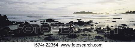 Picture - Young woman leaning against a rock on the beach. Fotosearch
