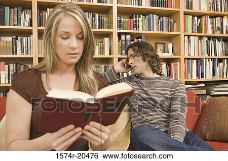 Young woman reading a book with a young man talking on a mobile phone in the background View Large Photo Image Stock Photograph - Young woman reading a book with a young man talking on a mobile phone in the background. Fotosearch