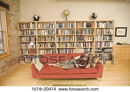Young woman reclining on a couch and reading a book View Large Photo Image Picture - Young woman reclining on a couch and reading a book. Fotosearch