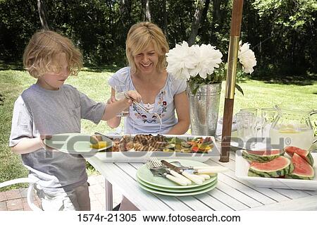 Young woman sitting at a table with her son choosing food from a tray View Large Photo Image Stock Photography - Young woman sitting at a table with her son choosing food from a tray. Fotosearch