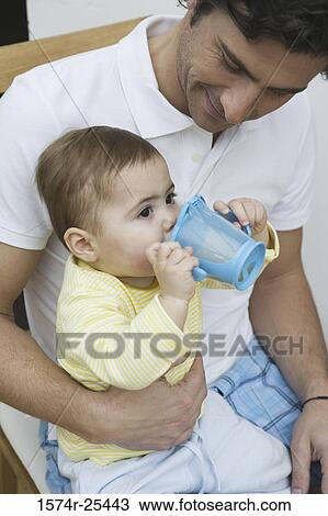 Stock Image - Baby boy sitting on his father's lap and drinking. Fotosearch