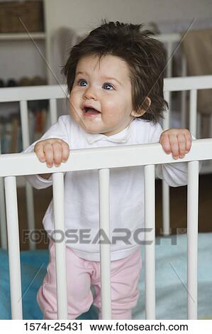 Baby girl standing in a crib View Large Photo Image Stock Image - Baby girl standing in a crib. Fotosearch