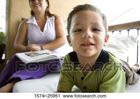 Boy lying on the bed with his mother sitting behind him View Large Photo Image Stock Image - Boy lying on the bed with his mother sitting behind him. Fotosearch