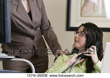 Stock Photo - Businesswoman holding a phone with a businesswoman standing beside her. Fotosearch