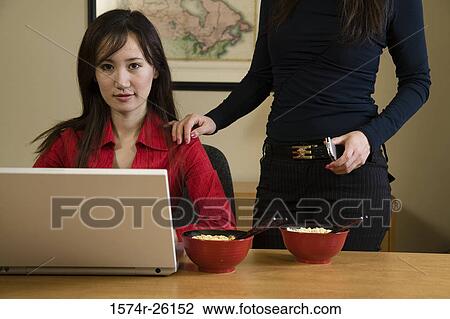 Stock Image - Businesswoman sitting in front of a laptop with another businesswoman standing beside her. Fotosearch
