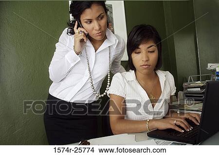 Businesswoman talking on a mobile phone and another businesswoman working on a laptop in an office View Large Photo Image Picture - Businesswoman talking on a mobile phone and another businesswoman working on a laptop in an office. Fotosearch