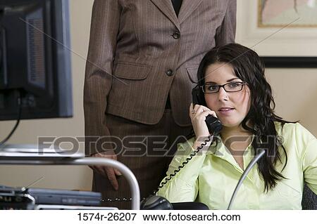 Stock Photo - Businesswoman talking on a phone with a businesswoman standing behind her. Fotosearch