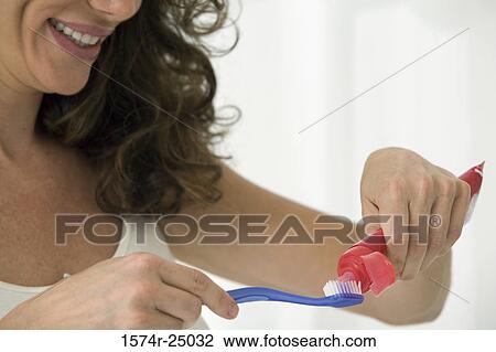 Stock Image - Close-up of a mid adult woman putting toothpaste on a toothbrush. Fotosearch