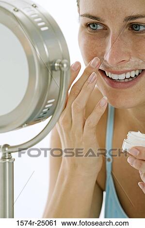 Close-up of a young woman applying cream to her face View Large Photo Image Stock Image - Close-up of a young woman applying cream to her face. Fotosearch