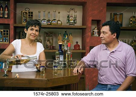 Female bartender pouring tequila into a glass with a mature man sitting at a counter in a cafe View Large Photo Image Stock Image - Female bartender pouring tequila into a glass with a mature man sitting at a counter in a cafe. Fotosearch