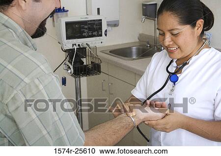 Stock Image - Female nurse checking the pulse of a patient and smiling. Fotosearch