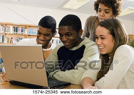 Four students sitting in front of a laptop in a library View Large Photo Image Stock Photography - Four students sitting in front of a laptop in a library. Fotosearch