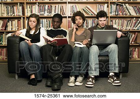Stock Image - Four students sitting on a couch in a library. Fotosearch