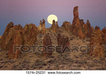Stock Image - Full moon rising over rock formations, Leslie Gulch, Oregon, USA. Fotosearch