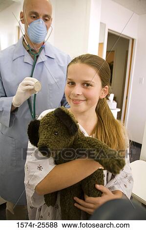 Girl holding a toy and a male doctor examining her View Large Photo Image Stock Photo - Girl holding a toy and a male doctor examining her. Fotosearch