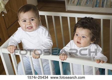 Picture - High angle view of a baby boy and baby girl standing in a crib. Fotosearch