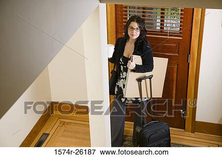 Stock Photo - High angle view of a businesswoman standing by a door with luggage. Fotosearch
