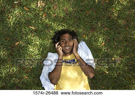 High angle view of a young man lying on grass and listening to music View Large Photo Image Stock Photo - High angle view of a young man lying on grass and listening to music. Fotosearch