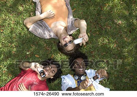 High angle view of three young men lying on grass and holding mobile phones View Large Photo Image Stock Image - High angle view of three young men lying on grass and holding mobile phones. Fotosearch