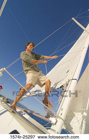 Low angle view of a young man standing on a sailboat and pulling a rope View Large Photo Image Stock Photo - Low angle view of a young man standing on a sailboat and pulling a rope. Fotosearch