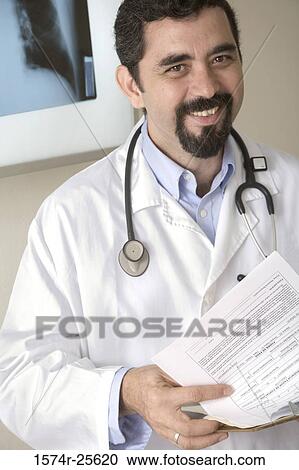 Male doctor holding a clipboard and smiling View Large Photo Image Stock Image - Male doctor holding a clipboard and smiling. Fotosearch