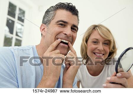 Mature man applying a teeth whitening strip to his teeth with a mid adult woman holding a mirror View Large Photo Image Stock Photo - Mature man applying a teeth whitening strip to his teeth with a mid adult woman holding a mirror. Fotosearch