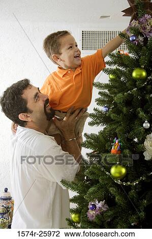 Stock Image - Mature man lifting his son to decorate a Christmas tree. Fotosearch