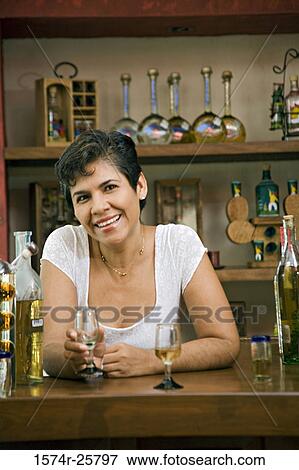 Stock Photo - Mature woman holding a glass of tequila and smiling. Fotosearch