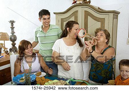 Stock Image - Mature woman playing a bugle with her family at a dining table. Fotosearch