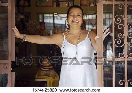 Stock Image - Mature woman standing at the door of a souvenir store and smiling. Fotosearch