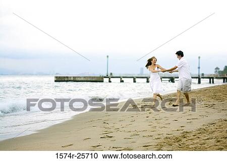 Mid adult man and a young woman holding each other's hands and running on the beach View Large Photo Image Stock Image - Mid adult man and a young woman holding each other's hands and running on the beach. Fotosearch