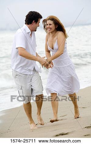 Mid adult man and a young woman holding each other's hands and running on the beach View Large Photo Image Stock Image - Mid adult man and a young woman holding each other's hands and running on the beach. Fotosearch