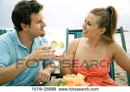Stock Photo - Mid adult man and a young woman toasting on the beach. Fotosearch