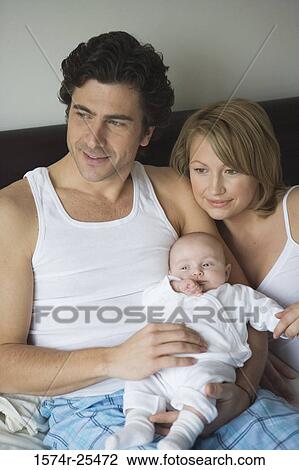 Mid adult man holding his baby with a mid adult womand sitting beside him View Large Photo Image Stock Image - Mid adult man holding his baby with a mid adult womand sitting beside him. Fotosearch