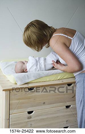 Stock Image - Mid adult woman bending over her baby on a changing table. Fotosearch