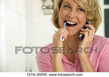 Mid adult woman brushing her teeth and using a mobile phone View Large Photo Image Stock Image - Mid adult woman brushing her teeth and using a mobile phone. Fotosearch