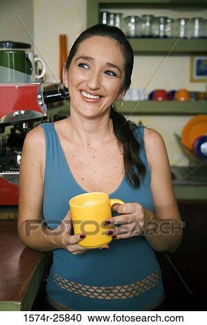 Mid adult woman holding a cup of coffee and smiling in a cafe View Large Photo Image Stock Image - Mid adult woman holding a cup of coffee and smiling in a cafe. Fotosearch